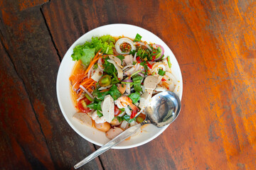 Food of Thailand Spicy mixed salad. Consisting of vegetables, shrimp, pork roll, squid and sausage. Place on a white plate and place on a wooden surface.
