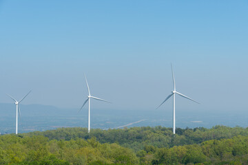 Travel in Thailand. Landmark of Khao Yai Thieng Windmill Nakhon Ratchasima Thailand. Wind turbines tower over a lush forest. Background of mountain far away under blue sky.