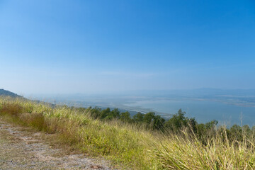 Viewpoint with ground and grass growing on the green edge. View of Lam Takhong Reservoir and the distant blurry mountain range.