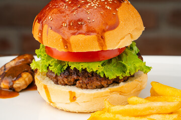 Delicious hamburger with homemade beef, tomato and lettuce. Served on a plate with French fries and mushrooms.