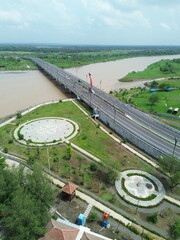 Aerial photograph showing a highway bridge spanning a wide river, surrounded by lush green...