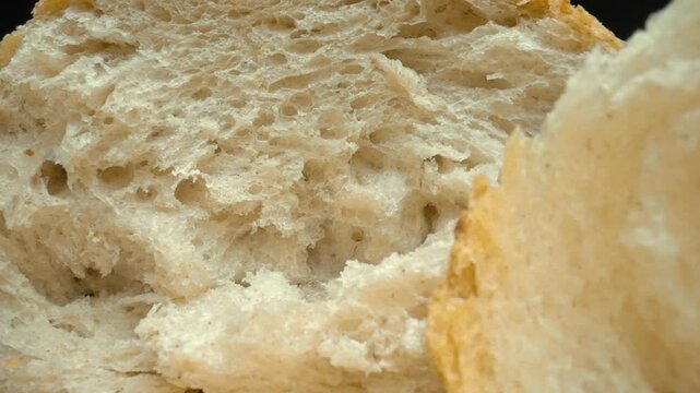 Close up of torn pieces of fresh baguette close-up on dark background. Macro photography of fres bread placed on wooden tray. Zoom in and rotating camera motion. Gourmet and bakery concept. Pabulum.
