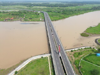 Aerial photograph showing a highway bridge spanning a wide river, surrounded by lush green...