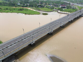 Aerial photograph showing a highway bridge spanning a wide river, surrounded by lush green...
