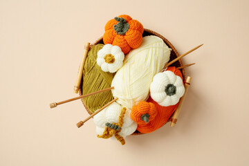Colorful yarn balls and knitted pumpkins in a basket with wooden knitting needles