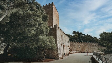 Scenic view of a historic stone castle wall surrounded by lush trees in Erice, Sicily, Italy