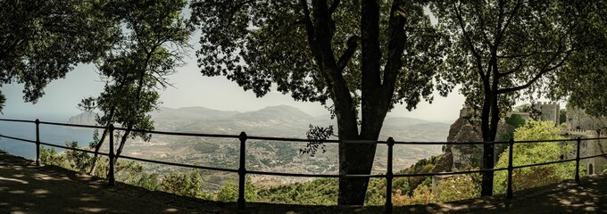 Panoramic view of a scenic landscape framed by trees and a railing in Erice, Sicily, Italy
