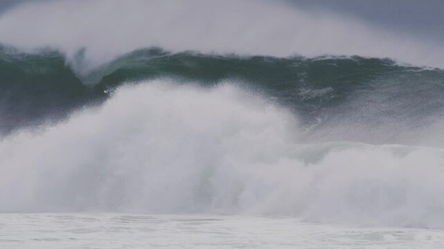 Slow motion shot of a large wave barreling, mist streaming off the top in stormy blue light