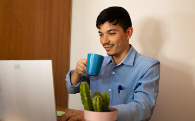 Businessman holding a blue cup of coffee while working on his laptop in the office in the morning