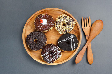 Donuts with different types of topping served on wooden plate, top view on black background. High resolution photo.