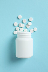 Various pills pouring out of a medicine bottle on a color background