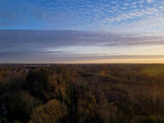 Aerial view of a serene autumn landscape with a vast forest under a partly cloudy sky during sunset