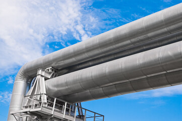 The photo shows pipeline lines against the backdrop of blue sky and clouds