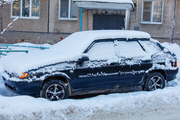 A black car covered in snow sits on a snowy road