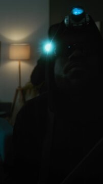 Vertical view of thief with headlamp holding crowbar glancing around living room, his accomplice with flashlight in background