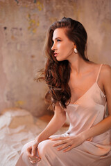 Naklejka premium A beautiful slender tall brunette in a silk beige dress. A magnificent portrait of a gorgeous girl with long hair down, stand on sand