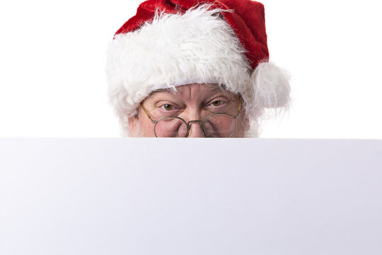 Christmas Santa Claus peeking over a blank white sign template looking at the camera viewer for holiday ad