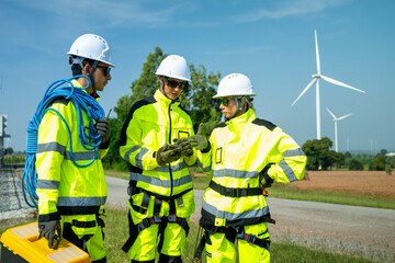 An engineer wearing safety gear closely inspects the base of a wind turbine in a renewable energy field.