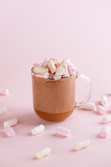 Hot chocolate cocoa drink with marshmallows, coconut milk and cinnamon in clear glass on a pink background. Vegan, sugar and lactose free. Vertical orientation.