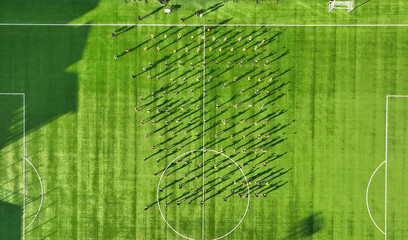 Aerial view of organized group shadows on green soccer field. This aerial photograph captures an organized group of people standing on a lush green soccer field, casting long, distinct shadows across