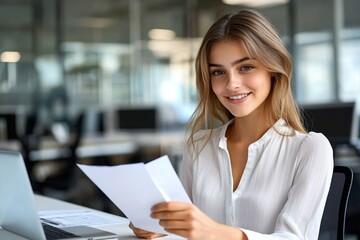 Fototapeta premium Young Woman Business Professional at Modern Office Desk Smiling Holding Paper and Working on Laptop
