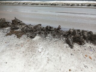 Dirty snow on the side of the road in the city. Car exhaust pollutes the air, the environment. Dust and soot lie on the snow along the highway in winter. Cleaning roads from snow.