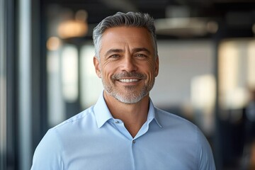 Obraz premium Smiling middle-aged businessman in office setting with gray hair and beard wearing dress shirt