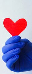 Hand in medical glove holds red paper heart. Postcard for doctor. International day of doctor, dentist, medical worker. Background.