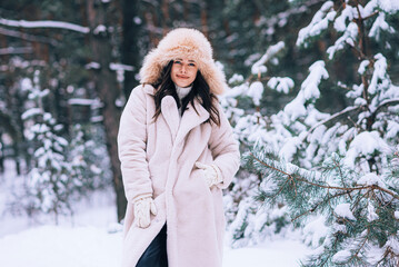 Young woman in snowy forest in winter. Portrait of happy woman playing with snow on sunny winter day. Walk in winter forest. Fun, relaxation concept.