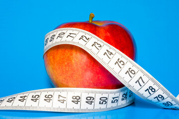 Red apple wrapped in measuring tape on blue background.