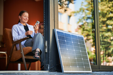 Happy woman using smartphone connected to photovoltaic solar panel. Sustainable renewable energy,...