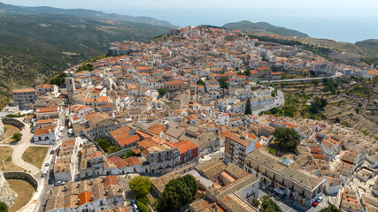 Aerial view of houses and buildings in the historic center of Monte Sant'Angelo, in the province of Foggia, Apulia. It is a typical village of Southern Italy. In background is the Mediterranean sea.