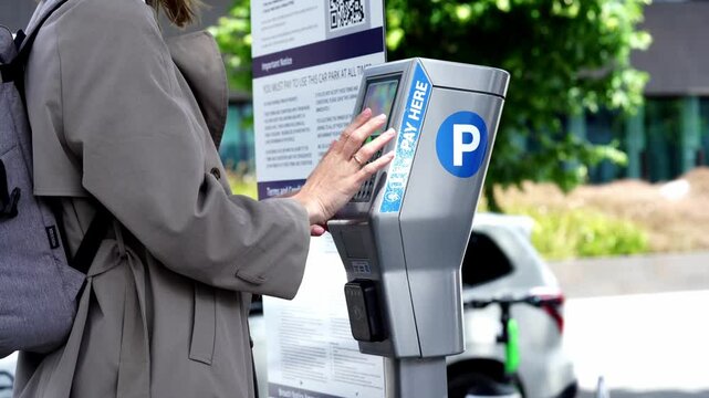 Young woman using a parking meter to pay for a car park in a city, New Zealand