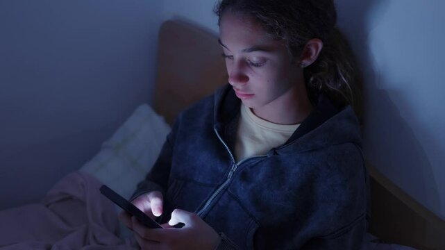 4K teenager girl using a smartphone lying in bed late at night, playing games, watching videos, and typing. Children's screen addiction. Screen Addiction in Youth