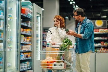 Couple checking shopping list on smartphone in supermarket