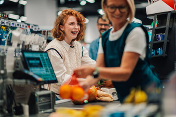 Cashier scanning groceries at checkout counter while customer is laughing