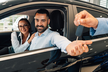 Charming couple grins while receiving car keys inside showroom