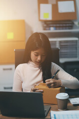 Startup SME small business entrepreneur of freelance Asian woman wearing apron using laptop and box to receive and review orders online to prepare to pack sell to customers, online sme business ideas.