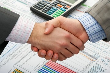 Business Professionals Shaking Hands Over Financial Documents and Calculator, Symbolizing Partnership and Collaboration in Corporate Environment