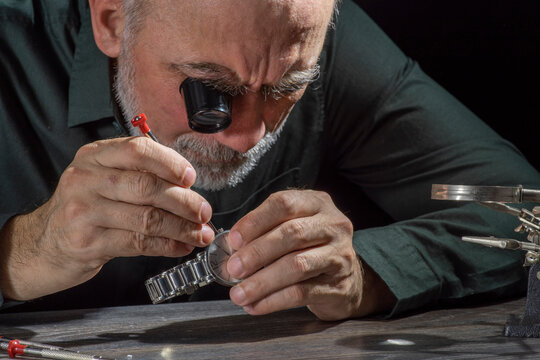 Watchmaker repairing watches looking through magnifying glass monocular. Professional senior watch fixer in repair services workshop.