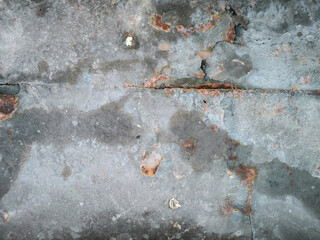 A grey and rusty surface with a few holes and cracks. The surface is rough and uneven, giving it a worn and aged appearance.