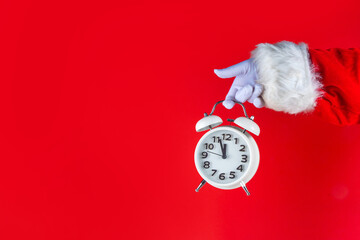 Santa Claus hand holding white alarm clock on red background