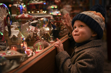 boy in hat looks from street at shop window of Christmas toys on Christmas