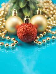 Red and golden decoration balls and golden beads garland and small green tree on a blue reflective surface. New Year and Christmas abstract background.