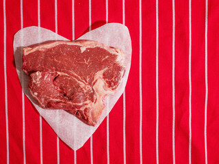 Fresh uncooked T bone steak on heart shaped cooking paper and on classic red and white stripe table...