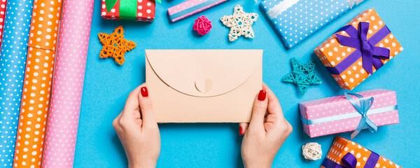 Obraz premium Top view of woman holding an envelope on blue background made of holiday decorations. Christmas time concept