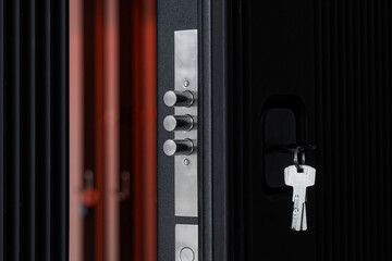 Keys in the keyhole and extended door lock bolts on an open black armored entrance door. Opening...