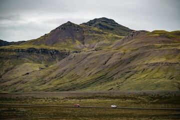 Cars on a remote road with rugged mountain backdrop.