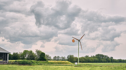 Rural landscape with the typical small EAZ farm wind turbine under cloudy sky, Netherlands. The wind mill company is under threat of bankruptcy. © VeugerStock