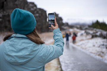 Mujer de espaldas haciendo foto y video con teléfono movil en paisaje con nieve con personas...